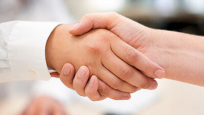 Zwei Personen geben sich zur Begrüßung die Hand.