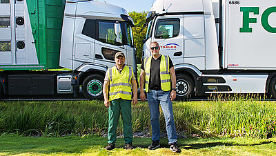 Zwei Wetralog-Fahrer in Warnwesten stehen vor einem Tiertransport-Lkw und einem Kühlfahrzeug.