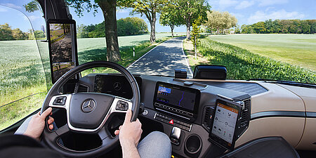 Blick aus einem modernen Lkw-Cockpit auf eine Landstraße mit digitalen Navigations- und Assistenzsystemen.