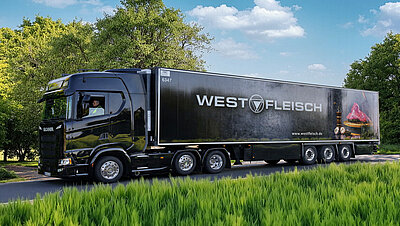 Schwarzer Westfleisch-Sattelzug fährt auf einer Landstraße durch eine grüne Landschaft.