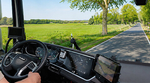 Lkw-Fahrer am Steuer einer modernen Fahrerkabine auf einer baumgesäumten Landstraße.