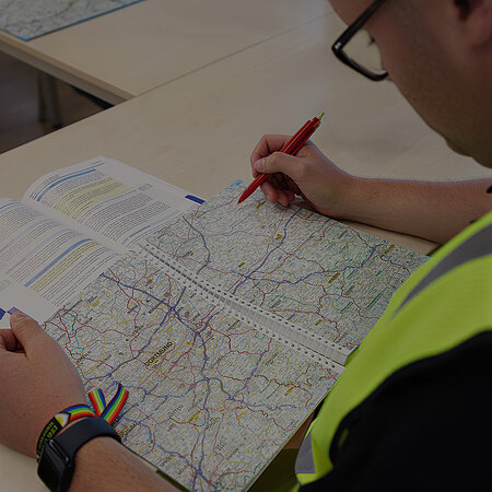 Person in Warnweste plant mit einem roten Stift eine Route auf einer Straßenkarte.