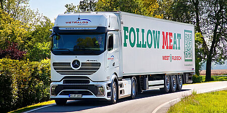 Weißer Wetralog-Kühl-Lkw mit Westfleisch-Kampagnenmotiv fährt auf einer Landstraße.
