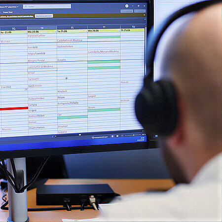Wetralog-Mitarbeiter mit Headset vor einem Monitor mit digitaler Tourenübersicht.