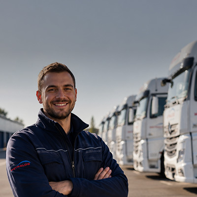 Lächelnder Wetralog-Mitarbeiter vor einer Reihe weißer Lkw.