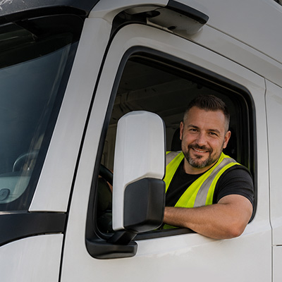 Lächelnder Wetralog-Lkw-Fahrer in Warnweste am geöffneten Seitenfenster der Fahrerkabine.